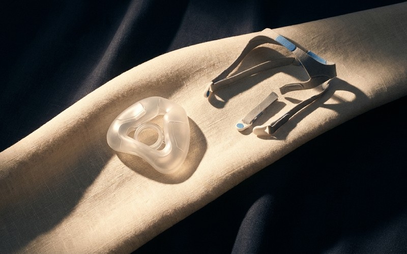 A CPAP nasal mask cushion and headgear straps laid out on light linen fabric.