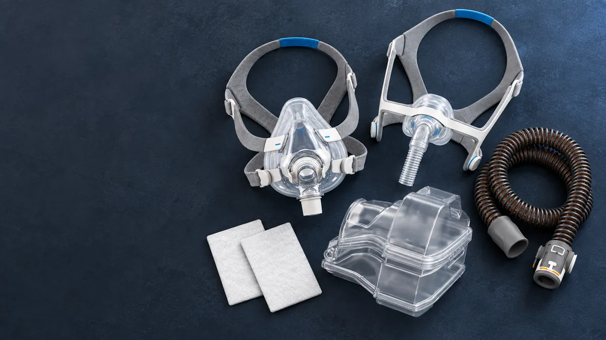 CPAP masks, headgear, coiled tubing, humidifier chamber and replacement filters laid out on a dark surface